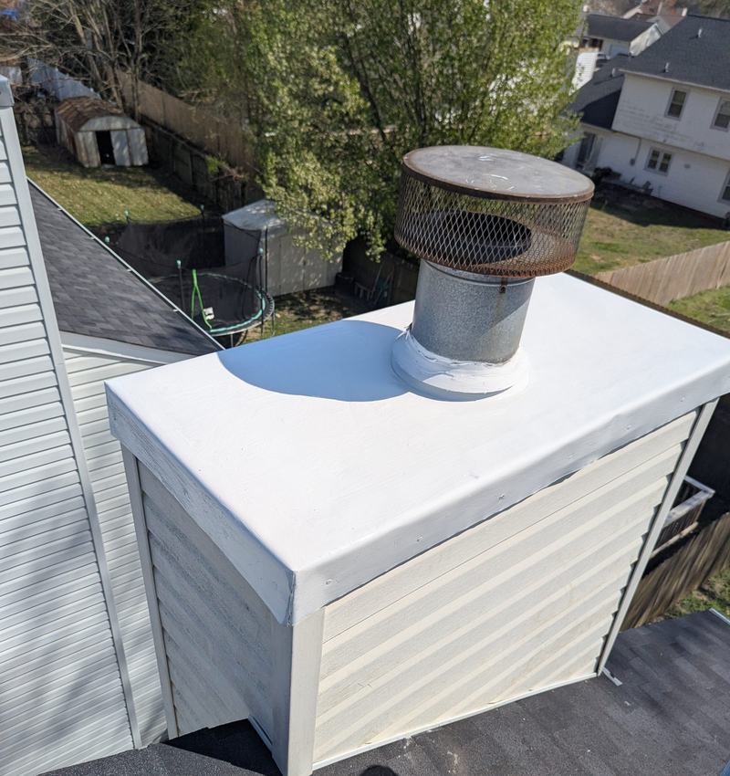 White chimney chase cover with metal flue cap above dark gray shingles