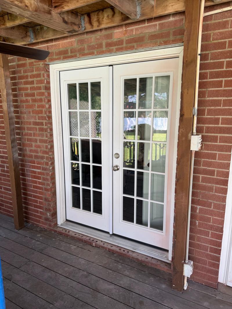 White double French doors with grid glass set into a red brick wall on a covered deck