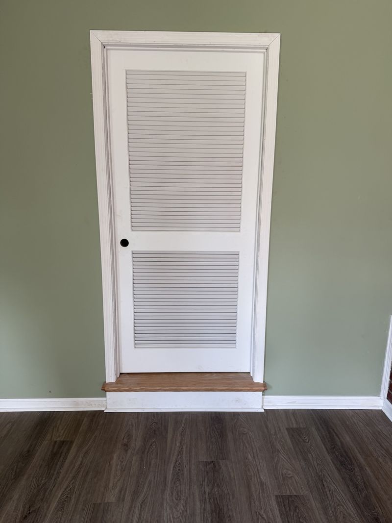Finished interior room with green walls, dark flooring, and white louvered door