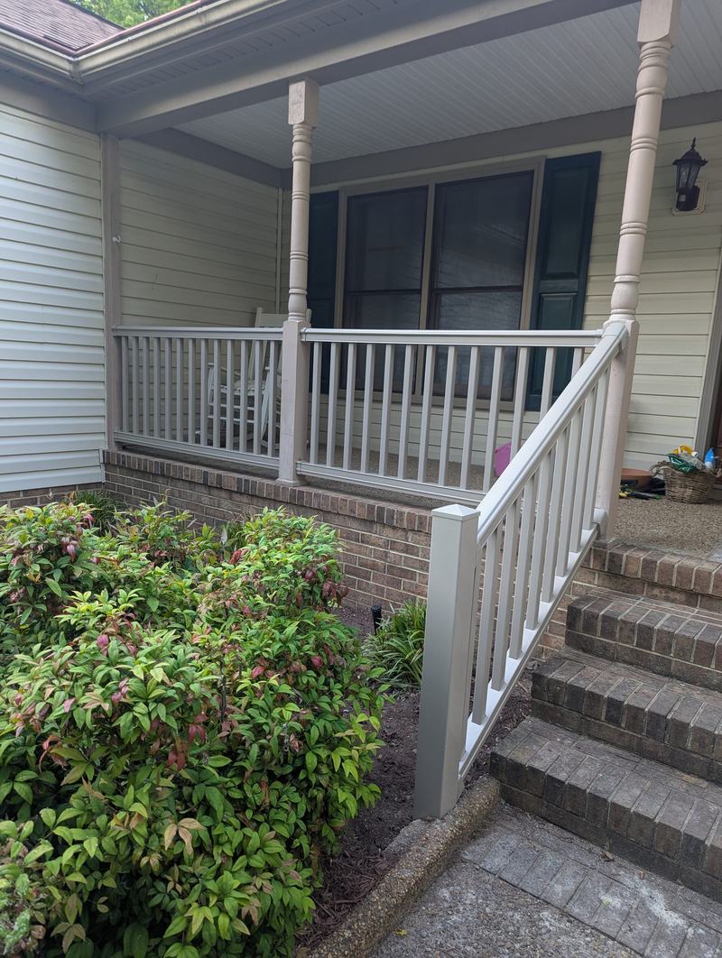 White vinyl porch railing and stair handrail over brick steps beside green shrubs