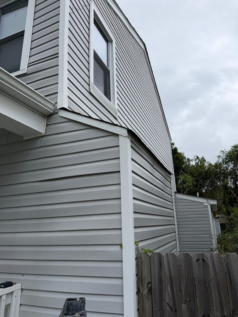 Gray vinyl siding corner with new white trim finishing the second-story overhang