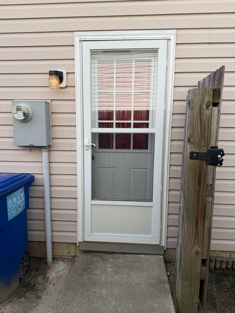 White storm door with glass panel and blinds behind it on a tan-sided house