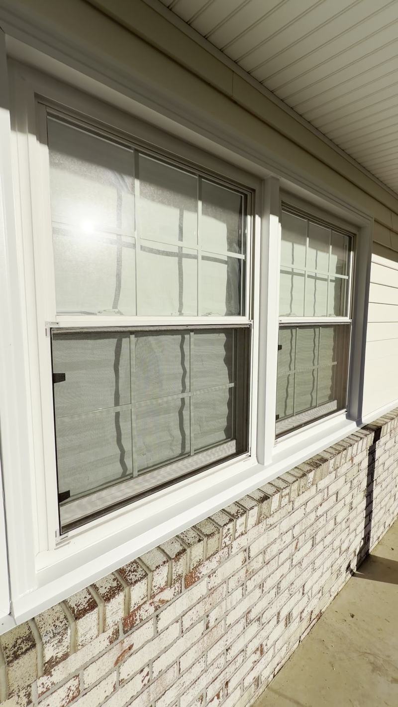 Pair of white double-hung windows with white exterior trim above a whitewashed brick wall